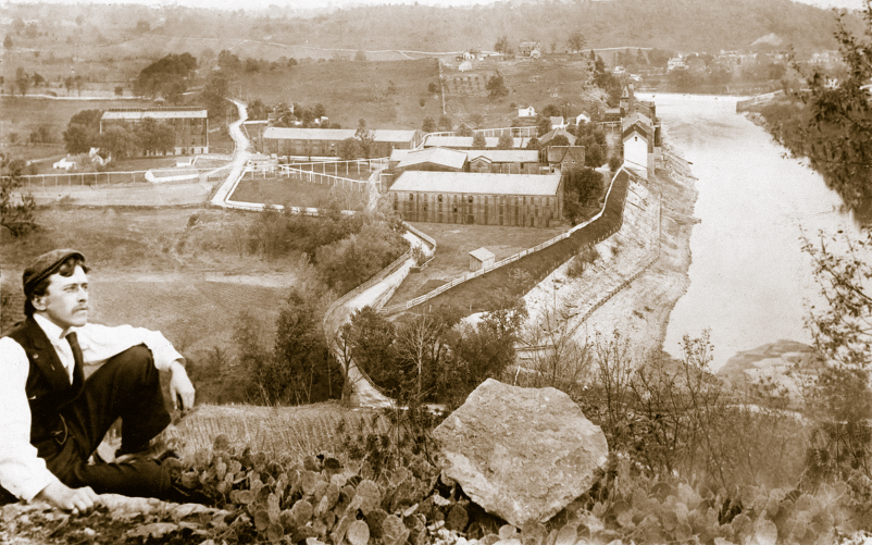 Vintage image of man on hilltop overlooking distillery on river